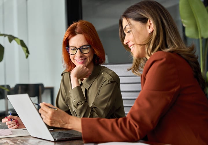 Two women talk in front of a laptop. 