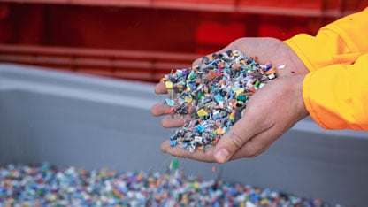 Open hands holding a scoop of loose plastic resin pellets