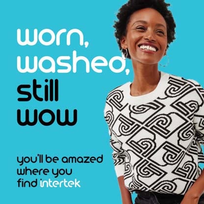 A woman smiling while wearing a white sweater with a distinct graphic pattern